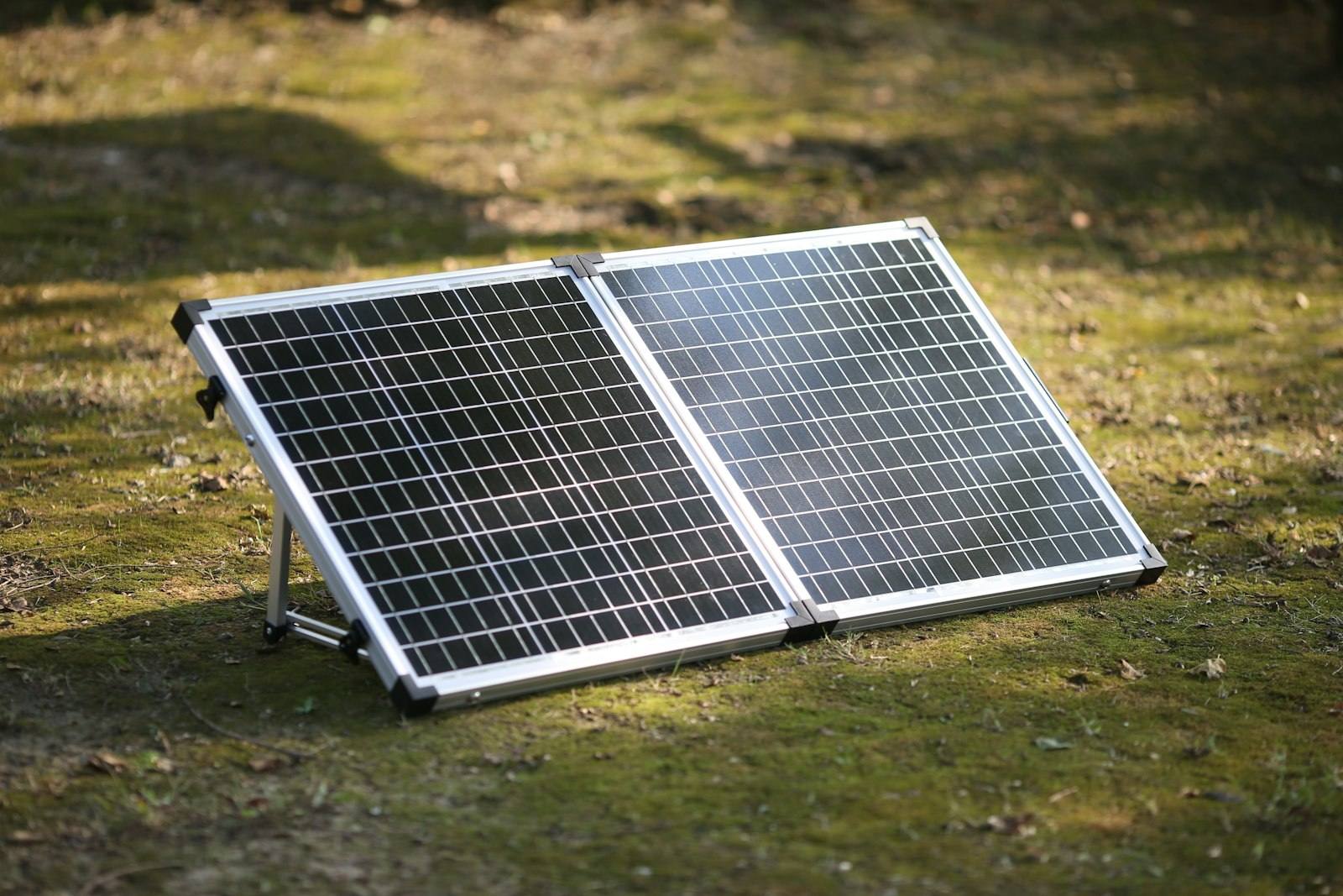 Panneau solaire pliant à cadre aluminium, déplié sur son pied dans l’herbe au soleil